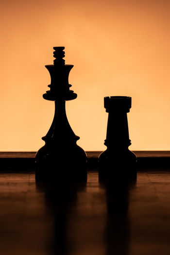 Close-up of silhouette chess on table against orange sky