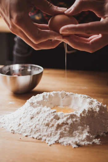 Midsection of man separating egg over flour on kitchen table