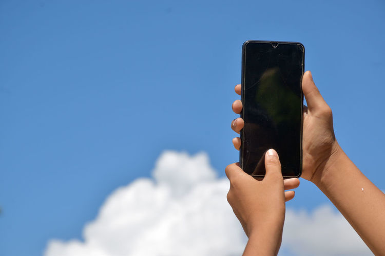 Midsection of person holding smart phone against blue sky