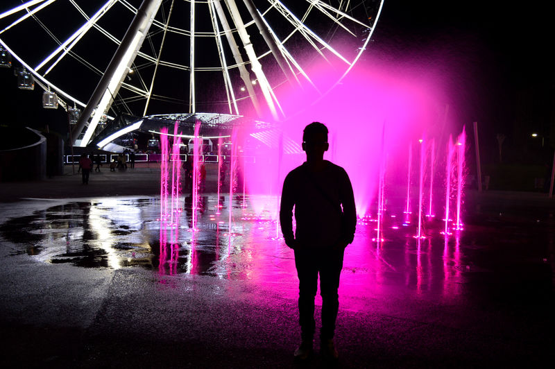 Silhouette man standing against pink illuminated fountain at night