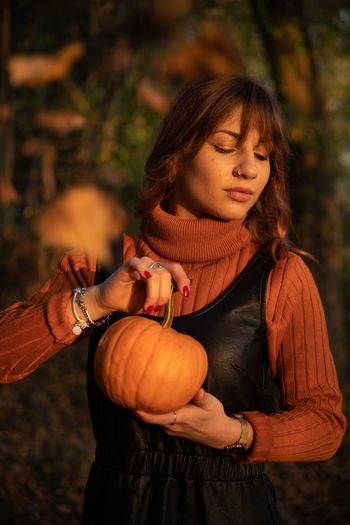 Young woman holding pumpkin while standing outdoors