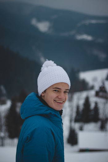 Candid portrait of a boy with childish joyful smile in a winter white hat and blue jacket.