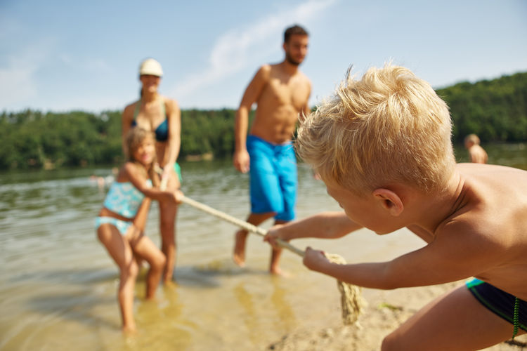 Siblings playing tug-of-war with parents in lake