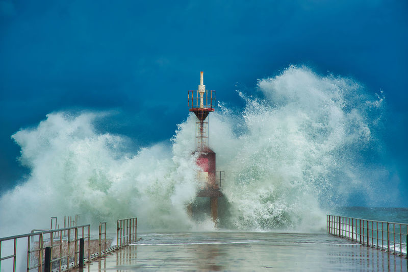 Waves splashing on lighthouse against blue sky