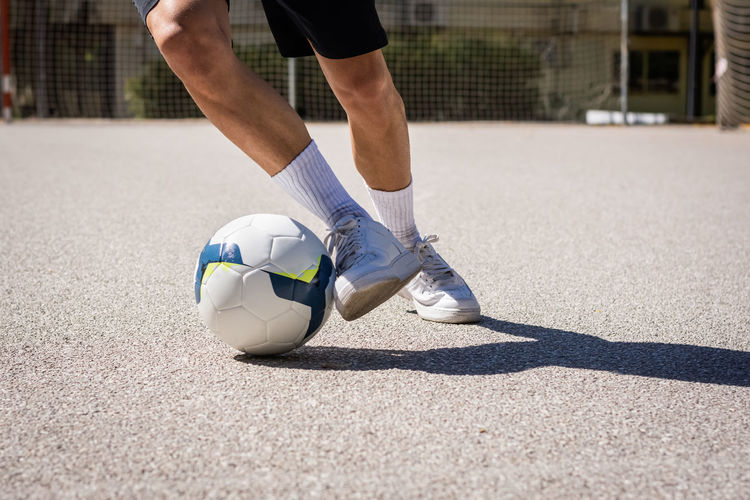 Cropped unrecognizable of male athlete with leg on soccer ball while practicing