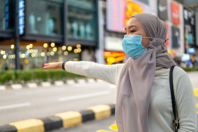 Young woman wearing mask gesturing while standing outdoors