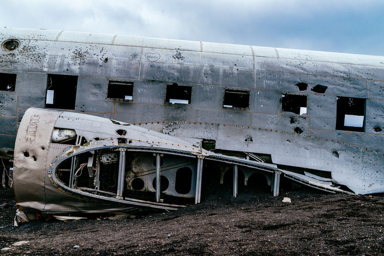 Abandoned military airplane at beach against cloudy sky during winter