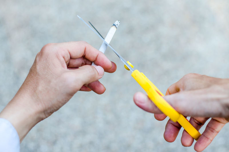 Cropped hands of man cutting cigarette with scissors 