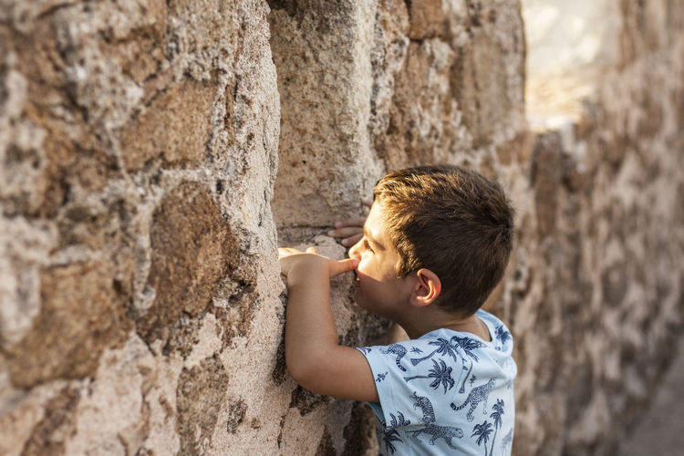 Side view of boy peeking through stone wall