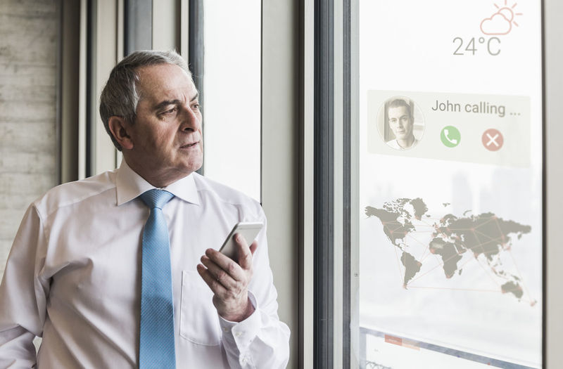 Businessman receiving a call on windowpane with world map in office