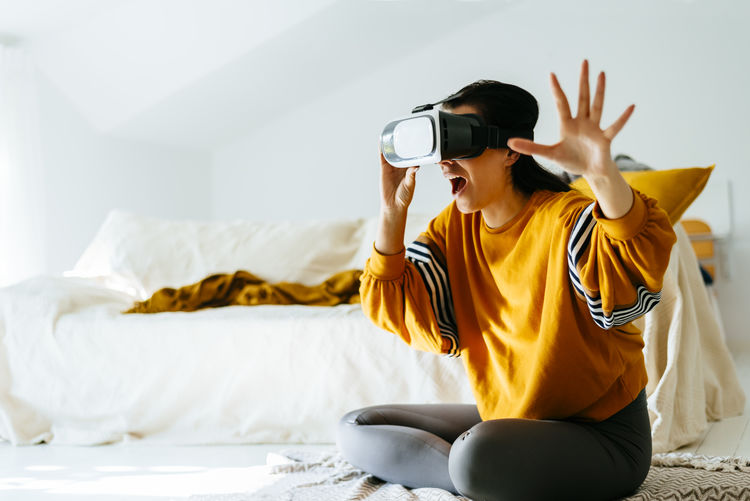 Woman wearing vr glasses sitting on bed