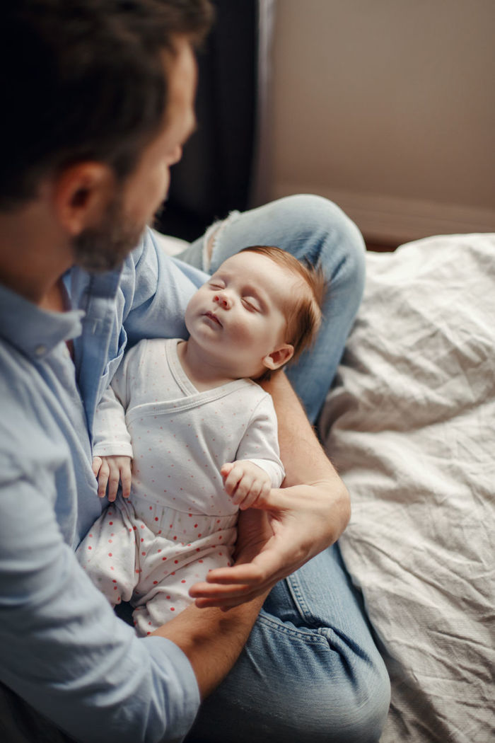 High angle view of father holding sleeping daughter while sitting on bed