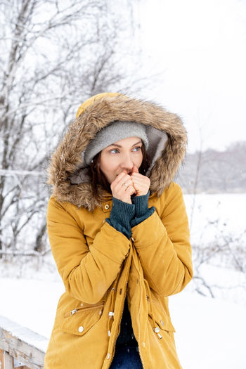 Thoughtful young woman sitting on railing in snow covered forest
