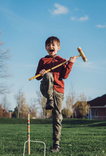 Young boy doing an excited jump while playing croquet outside.