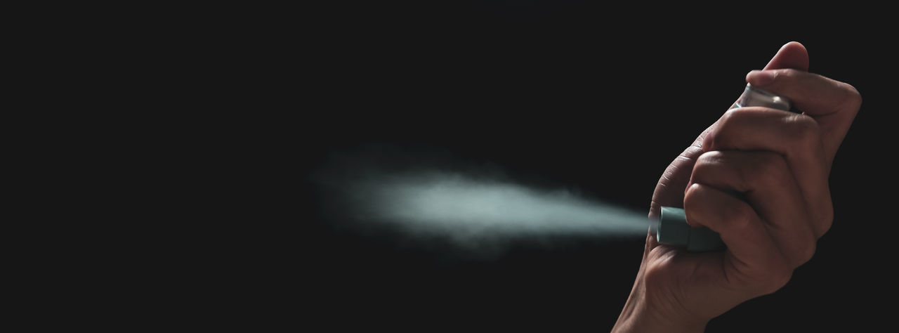 Close-up of hand holding asthma inhaler against black background