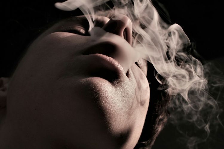 Close-up of man exhaling smoke against black background