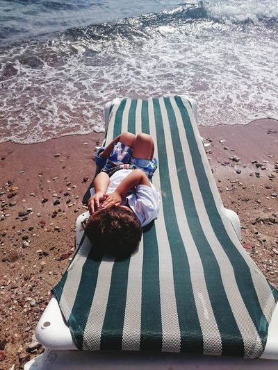 Full length of boy lying on lounge chair at beach during summer