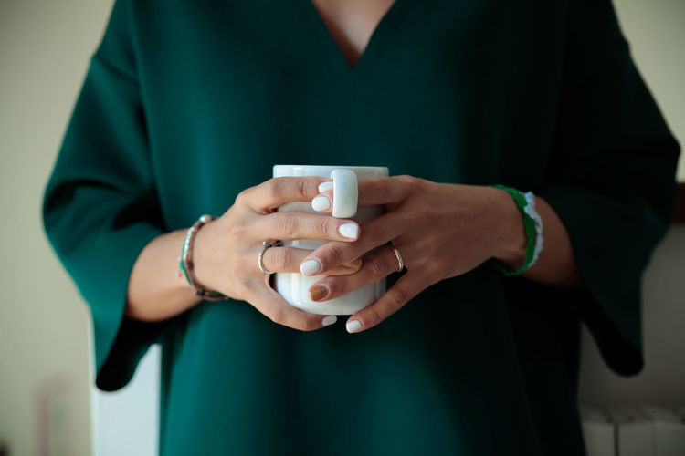 Midsection of young woman standing with cup at home