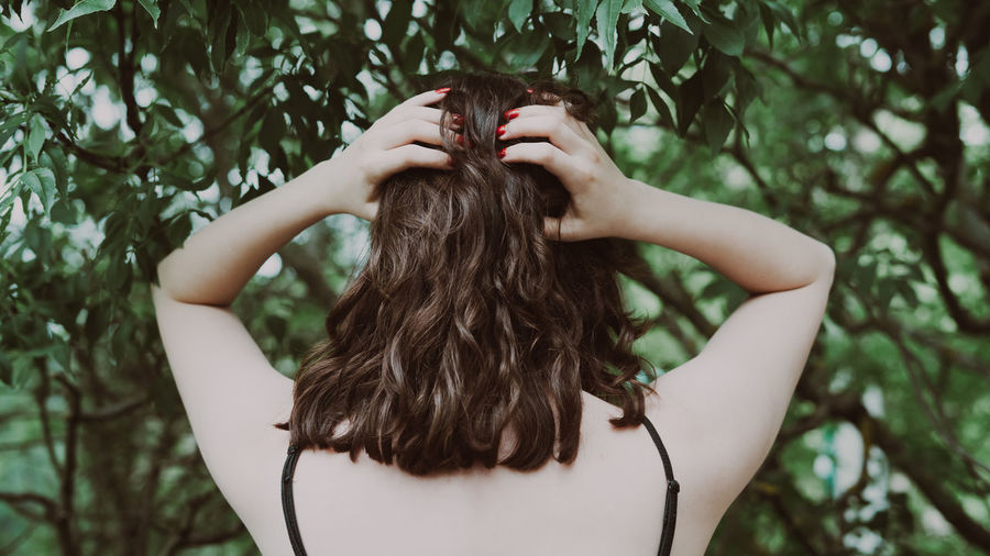Woman with curly brown hair from behind standing in a forrest