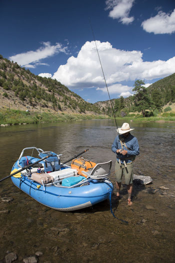 A fly fisherman prepares his gear while standing net to a raft.