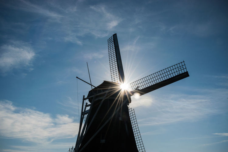 Low angle view of windmill silhouette against blue sky