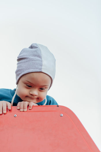 Cute little boy with down syndrome in hat walks in the playground, on children's slide