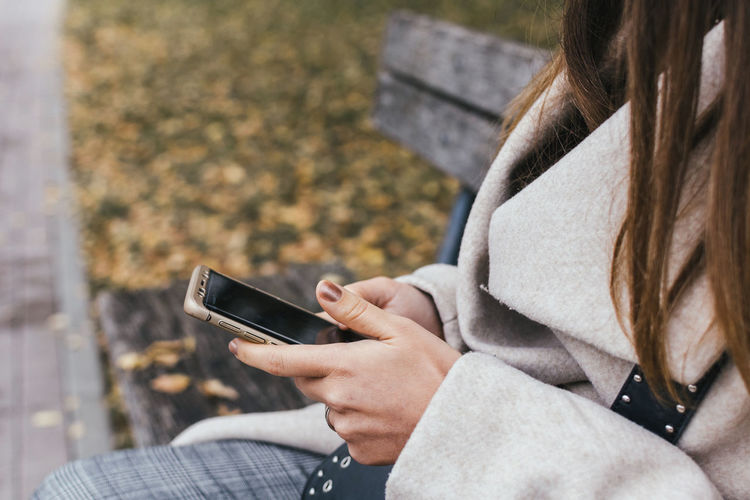 Midsection of woman using phone while sitting on bench
