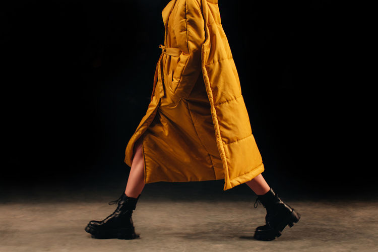 Female  figure in a long yellow fancy outfit and black boots walking the runway at the fashion week 