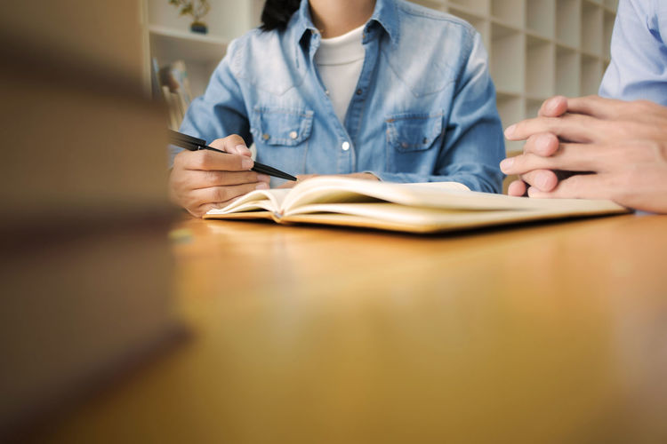 Midsection of business colleagues discussing over book at desk in office