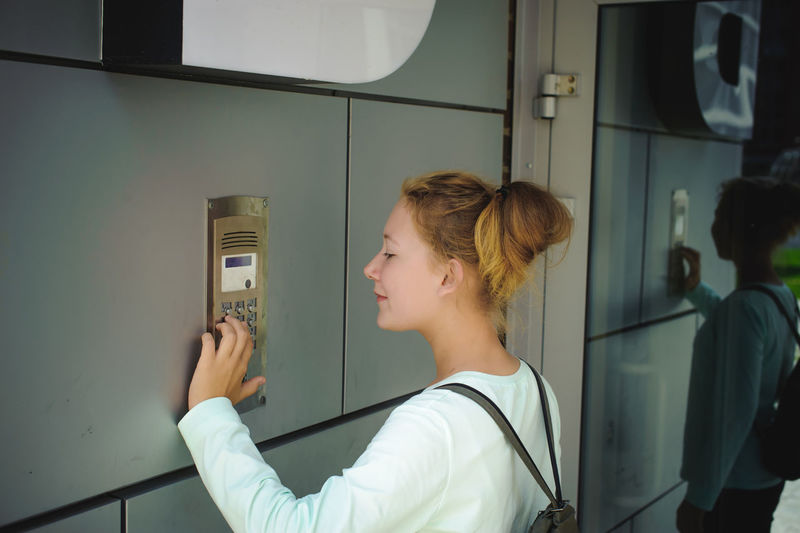 Side view of young woman using intercom