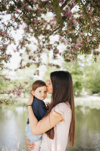 Mother and girl standing by tree against plants