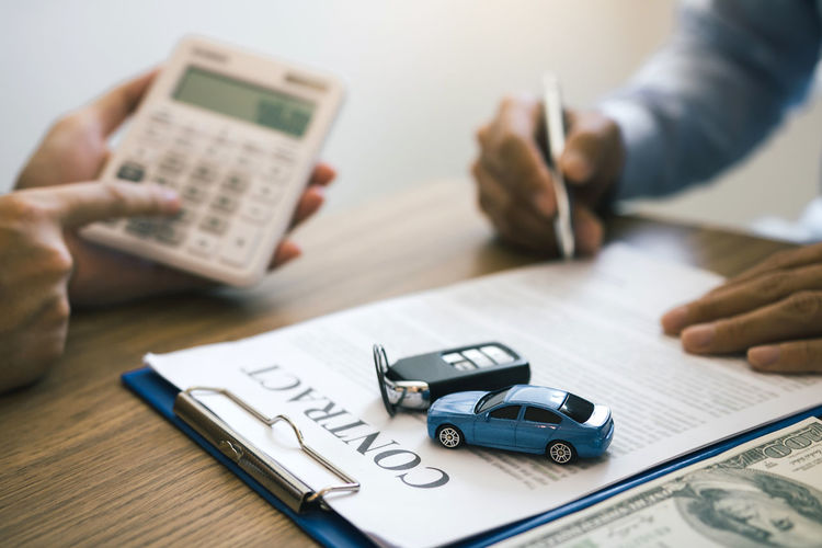 Cropped hands of customer signing contract with car salesperson sitting at desk