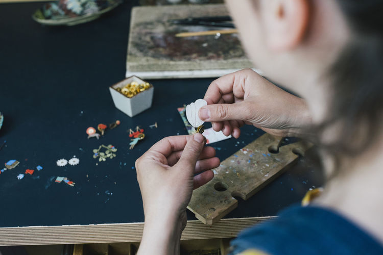 Hands of female craftsperson making jewelry on workbench