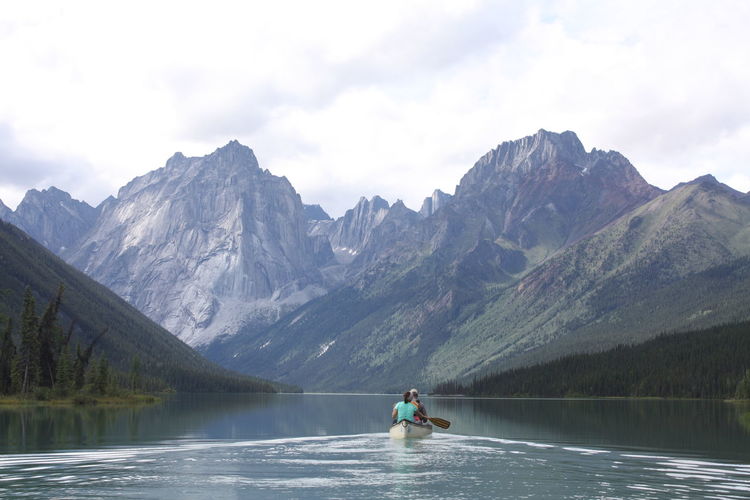 Couple canoeing on lake against mountains