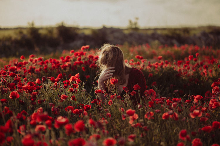 Midsection of woman with red flowers on field