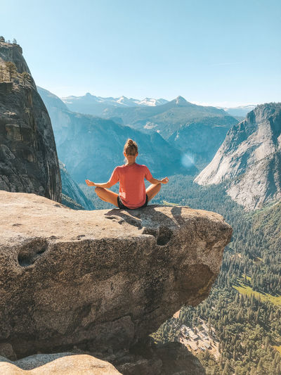 Rear view of woman meditating while sitting on rock