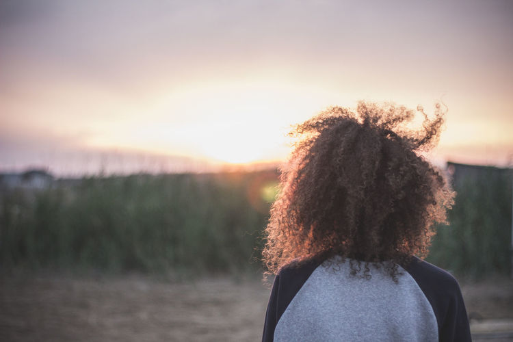 Rear view of woman with curly hair against sky during sunset