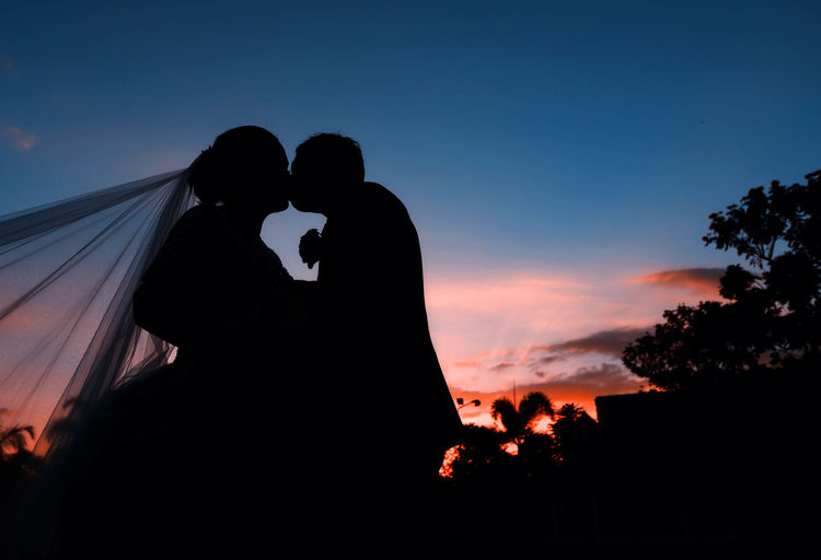 Low angle view of silhouette husband and wife against sky at dusk