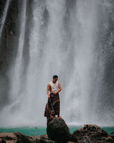 Man standing on rock against waterfall