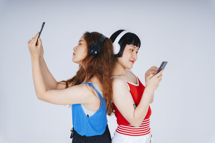 Lesbian couple using phone while listening music against gray background