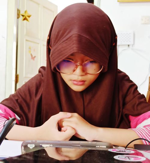 Close-up of girl wearing hijab using mobile phone on table