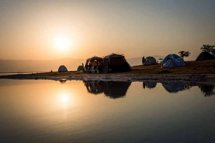 Tents by riverbank against sky during sunrise