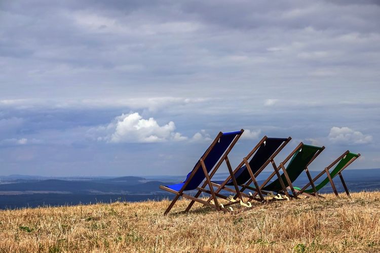 Deck chairs on field against sky