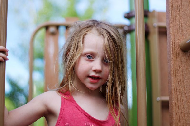 Close-up portrait of girl standing by outdoor play equipment
