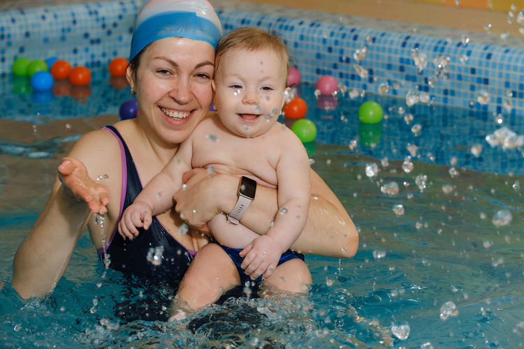 Early swimming coach training to swim baby boy in indoor pool. playing activity for infant with