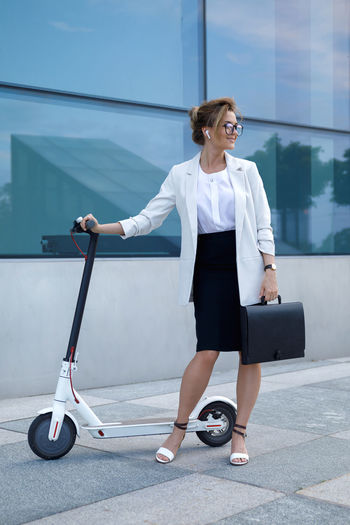 Full length of businesswoman standing by push scooter on street