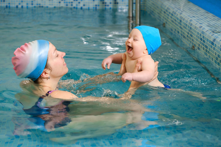 Early age swimming in pool. baby boy trained to swim in water. happy child with trainer woman in