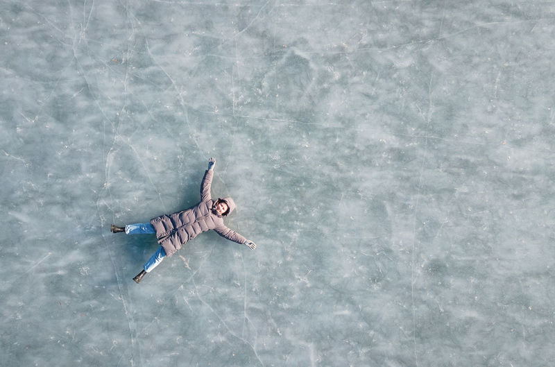 Young woman in a winter down jacket lies on frozen ice, top view