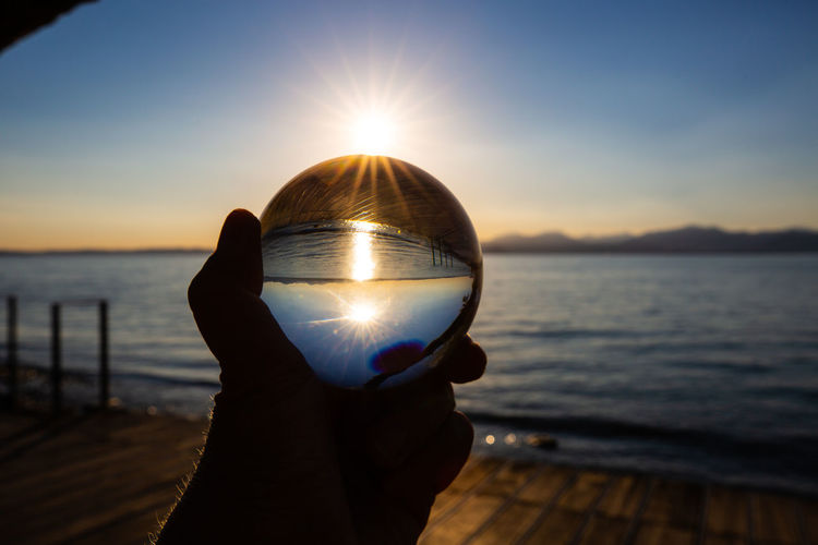 Cropped hand holding light bulb against sky during sunset