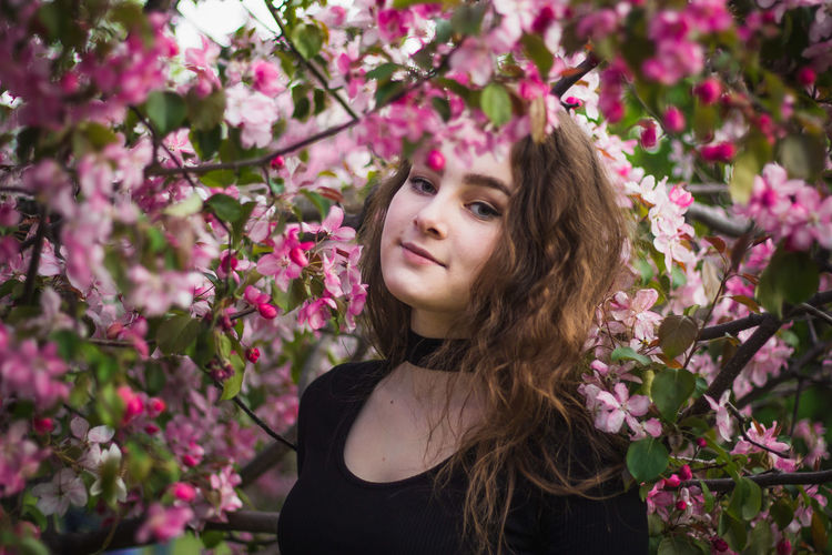 Close-up of beautiful young woman standing by pink flowers